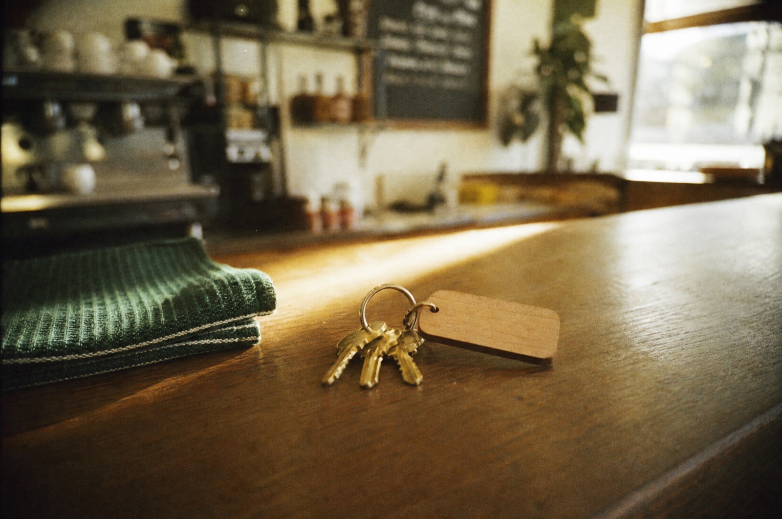 A ring of brass shop keys with a blank wooden tag lying on a café counter in a streak of morning sun